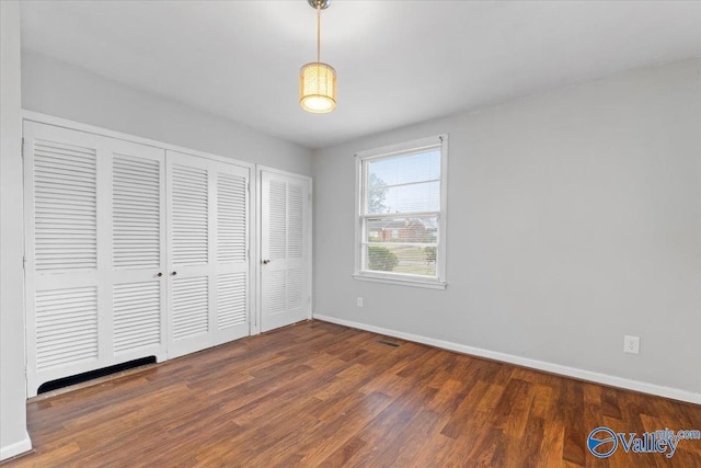 unfurnished bedroom featuring visible vents, a closet, baseboards, and wood finished floors