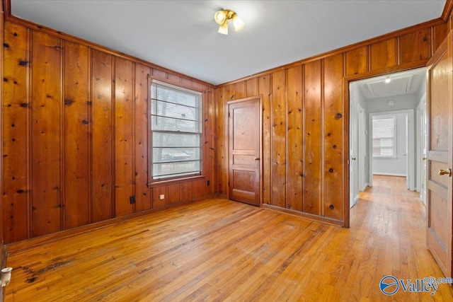 unfurnished room with baseboards, wood walls, attic access, and light wood-style floors