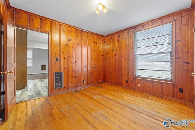 unfurnished room with light wood-type flooring, visible vents, wood walls, and heating unit