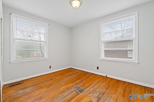 empty room with baseboards, visible vents, and wood finished floors