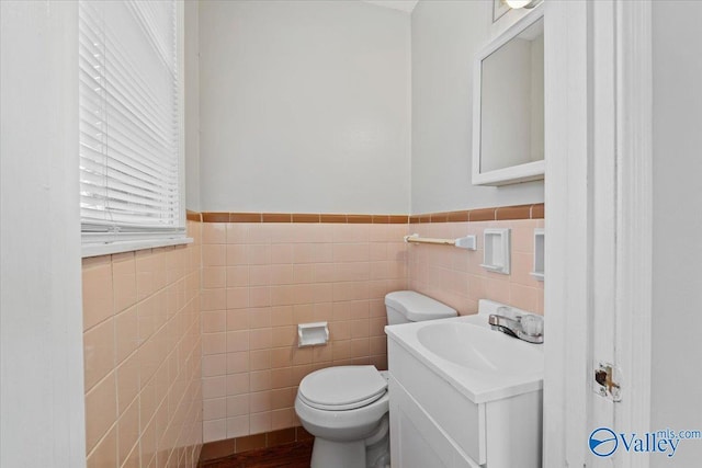 half bathroom with tile walls, a wainscoted wall, vanity, and toilet