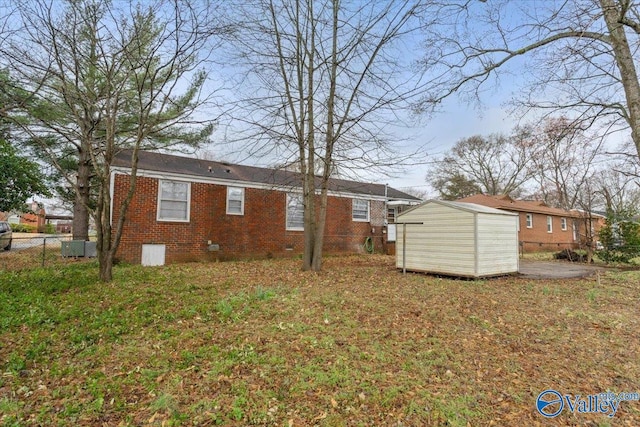 back of house featuring crawl space, a storage unit, an outdoor structure, and brick siding