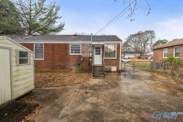 back of house with entry steps, an outbuilding, a gate, fence, and brick siding