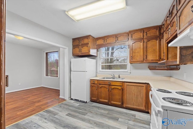 kitchen with white appliances, brown cabinetry, and a sink