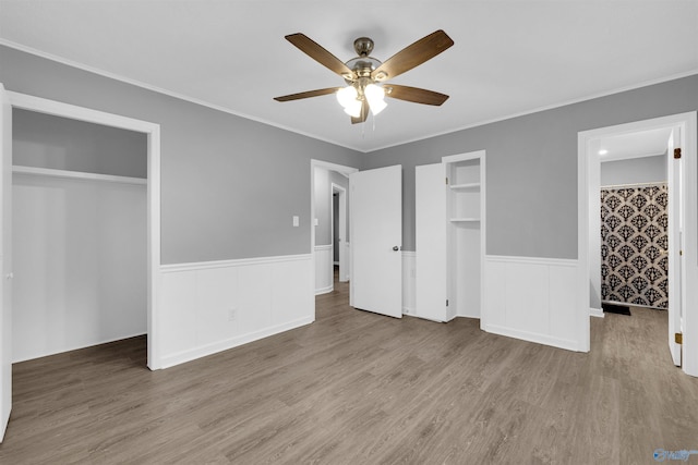 unfurnished bedroom featuring hardwood / wood-style floors, two closets, ornamental molding, and ceiling fan