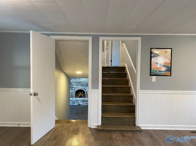 staircase with hardwood / wood-style floors, crown molding, and a brick fireplace