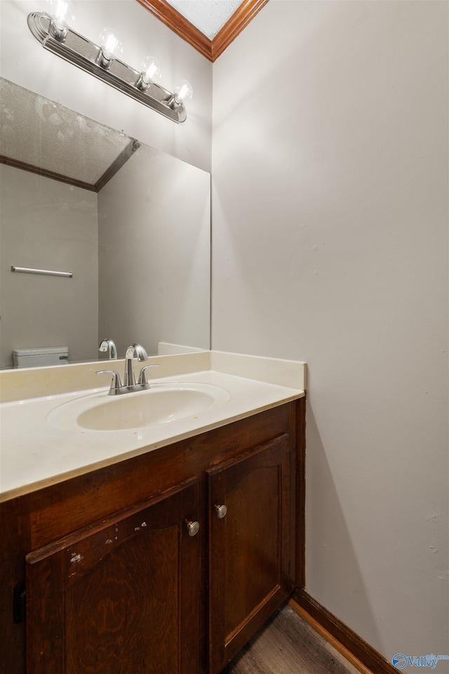 bathroom with toilet, vanity, wood finished floors, baseboards, and ornamental molding