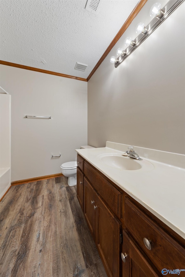 bathroom featuring vanity, ornamental molding, a textured ceiling, visible vents, and wood finished floors