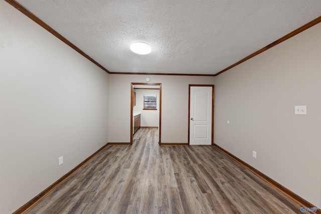 unfurnished room featuring baseboards, crown molding, wood finished floors, and a textured ceiling