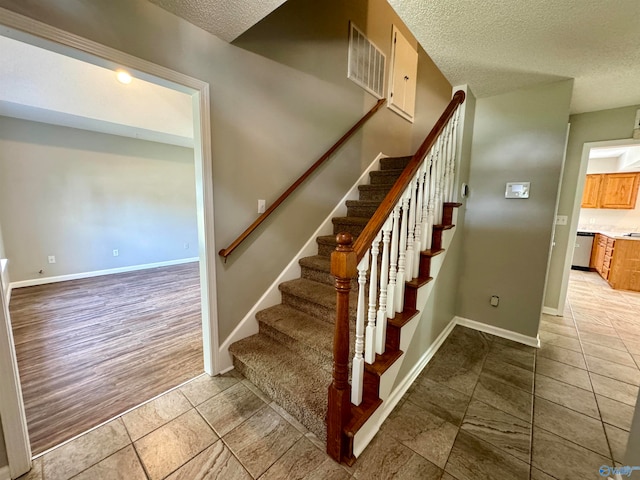 stairway with a textured ceiling and wood-type flooring