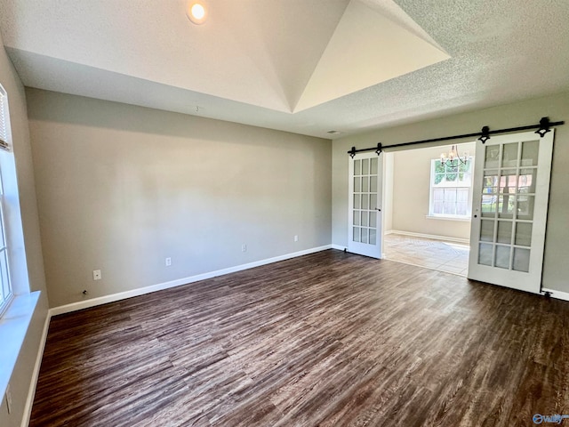 unfurnished room with a textured ceiling, a barn door, a notable chandelier, and wood-type flooring