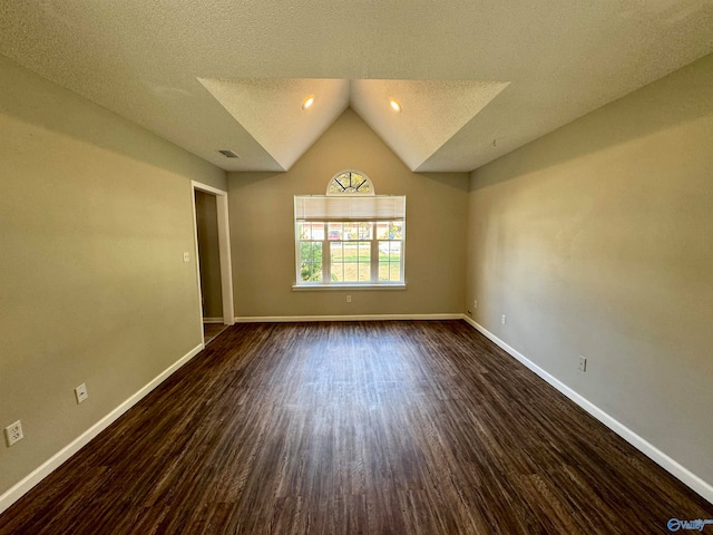 empty room with vaulted ceiling, dark hardwood / wood-style flooring, and a textured ceiling