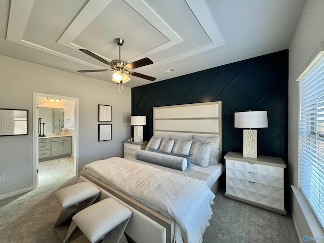 carpeted bedroom featuring a ceiling fan, baseboards, a tray ceiling, an accent wall, and connected bathroom