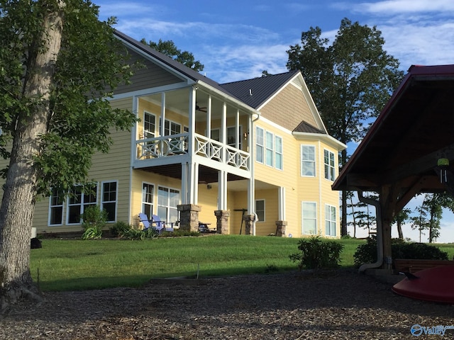 back of property with a yard, a balcony, and ceiling fan