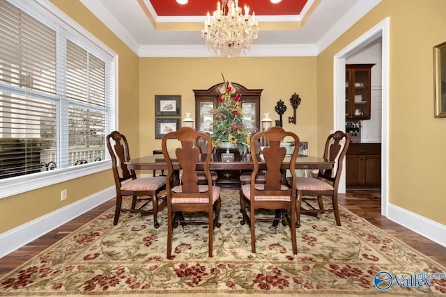 dining room with dark hardwood / wood-style flooring, a notable chandelier, a tray ceiling, and ornamental molding