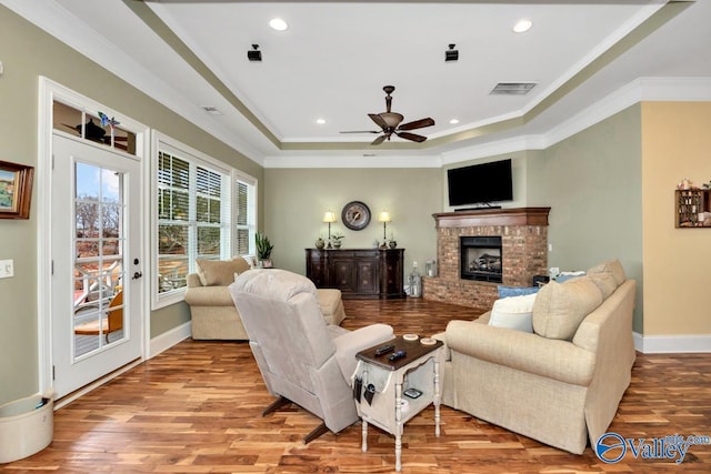 living room featuring crown molding, a tray ceiling, a brick fireplace, and light hardwood / wood-style flooring