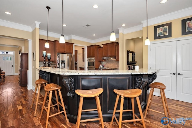 kitchen featuring a breakfast bar area, appliances with stainless steel finishes, hanging light fixtures, tasteful backsplash, and light stone countertops