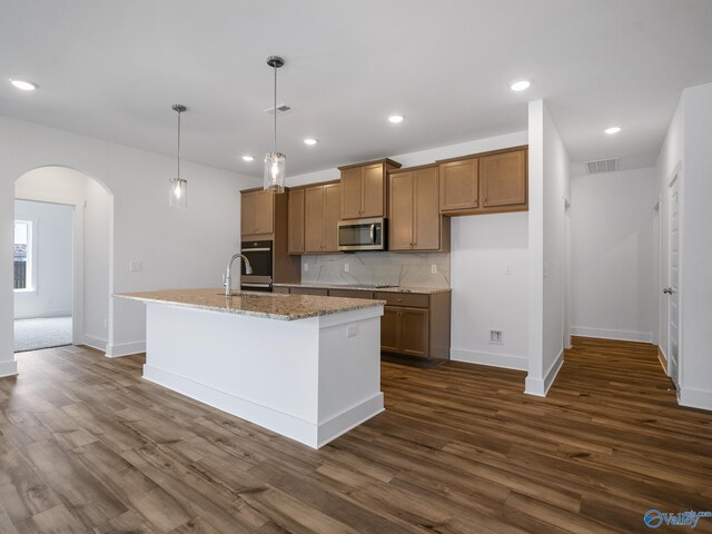 kitchen featuring a center island with sink, dark wood-type flooring, light stone countertops, and decorative light fixtures