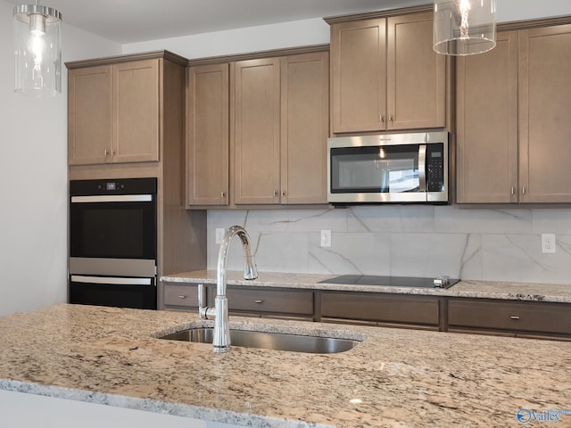 kitchen with light stone countertops, appliances with stainless steel finishes, sink, backsplash, and pendant lighting