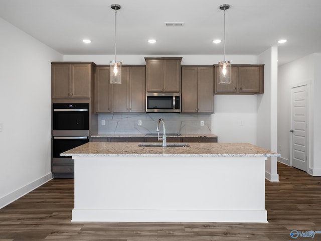 kitchen with appliances with stainless steel finishes, decorative light fixtures, sink, and an island with sink