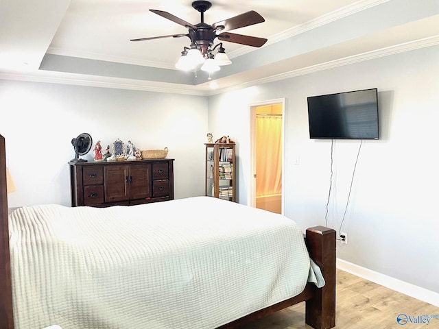 bedroom featuring ornamental molding, a raised ceiling, light wood-type flooring, ceiling fan, and ensuite bathroom