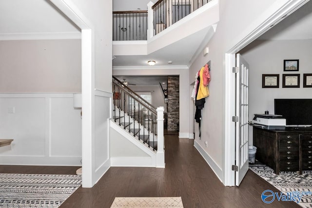 entryway featuring dark wood-type flooring, a towering ceiling, and ornamental molding