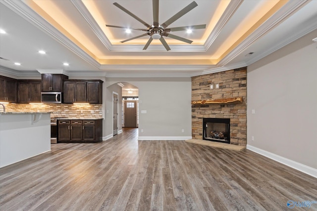 unfurnished living room featuring a tray ceiling, a stone fireplace, ornamental molding, and hardwood / wood-style flooring