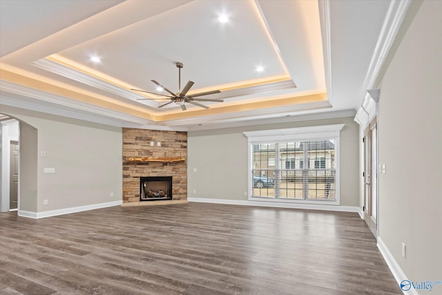 unfurnished living room featuring dark hardwood / wood-style flooring, a tray ceiling, a fireplace, and ceiling fan