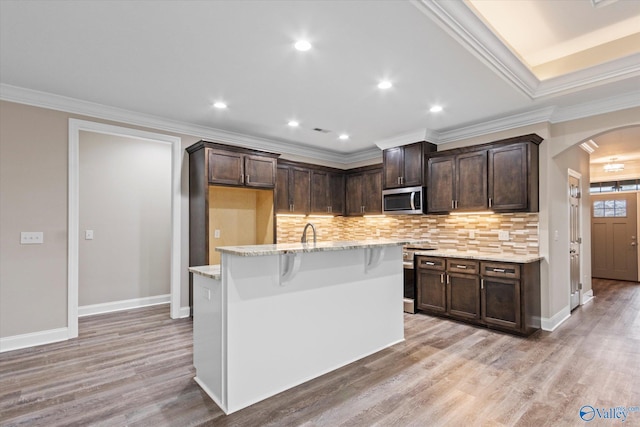 kitchen featuring dark brown cabinetry, light stone counters, a center island with sink, light wood-type flooring, and stainless steel appliances