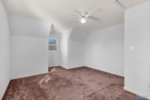 additional living space featuring ceiling fan, lofted ceiling, dark carpet, and a textured ceiling