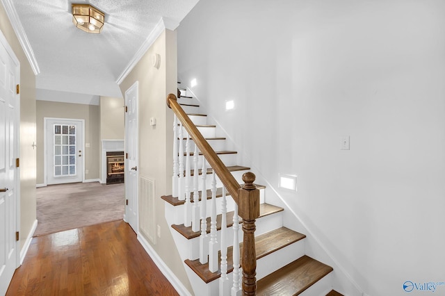 stairs with crown molding, a textured ceiling, and hardwood / wood-style flooring