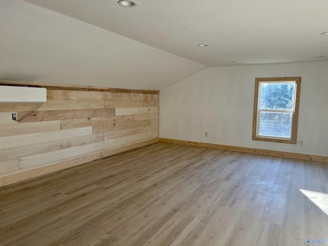 additional living space featuring vaulted ceiling, wood walls, light hardwood / wood-style flooring, and a wall mounted air conditioner