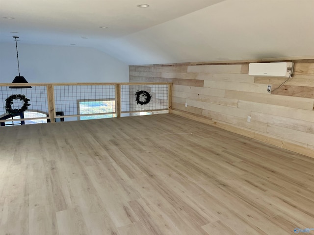 additional living space featuring an AC wall unit, wood walls, lofted ceiling, and light wood-type flooring