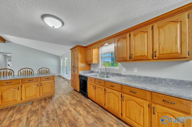 kitchen featuring dishwasher, a sink, light wood-type flooring, brown cabinets, and vaulted ceiling