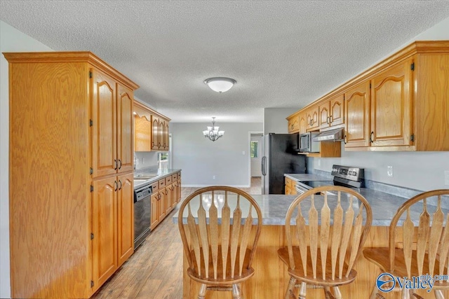 kitchen with light wood-type flooring, an inviting chandelier, a peninsula, a kitchen bar, and black appliances