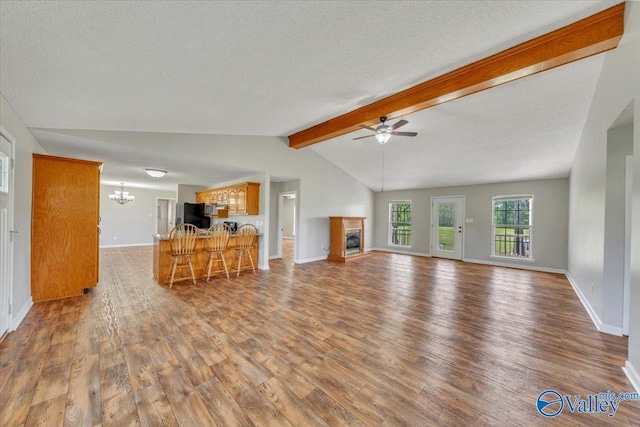 unfurnished living room with lofted ceiling with beams, a textured ceiling, wood finished floors, ceiling fan with notable chandelier, and a glass covered fireplace