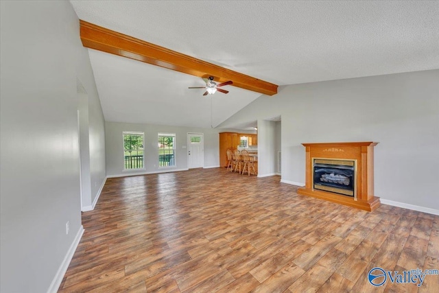 unfurnished living room with lofted ceiling with beams, ceiling fan, a textured ceiling, wood finished floors, and a glass covered fireplace