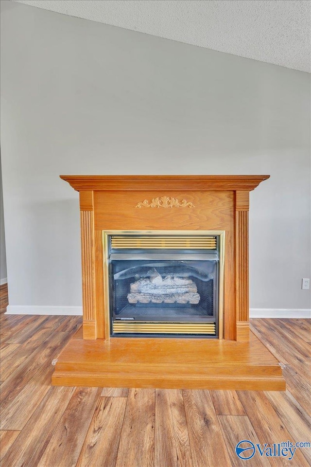 details featuring a fireplace, baseboards, a textured ceiling, and wood finished floors