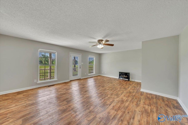 unfurnished living room featuring a textured ceiling, a ceiling fan, visible vents, wood finished floors, and baseboards