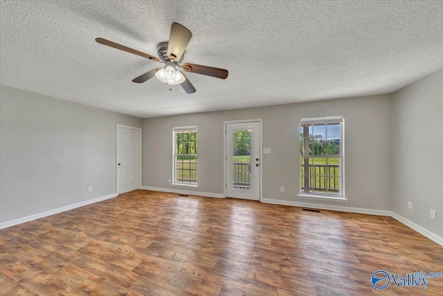 empty room with wood finished floors, ceiling fan, baseboards, and a wealth of natural light