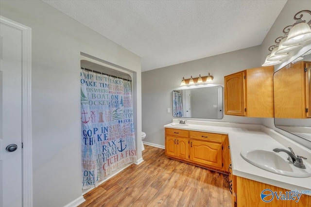bathroom with a sink, toilet, a textured ceiling, double vanity, and wood finished floors