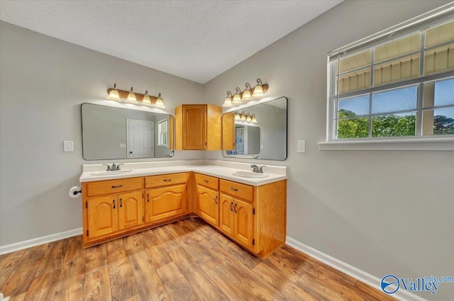 full bathroom with wood finished floors, double vanity, a sink, and baseboards