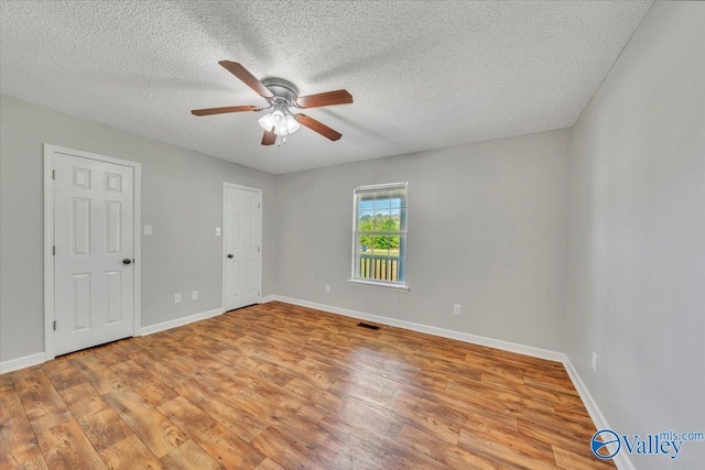 unfurnished room featuring baseboards, a textured ceiling, a ceiling fan, light wood-style floors, and visible vents