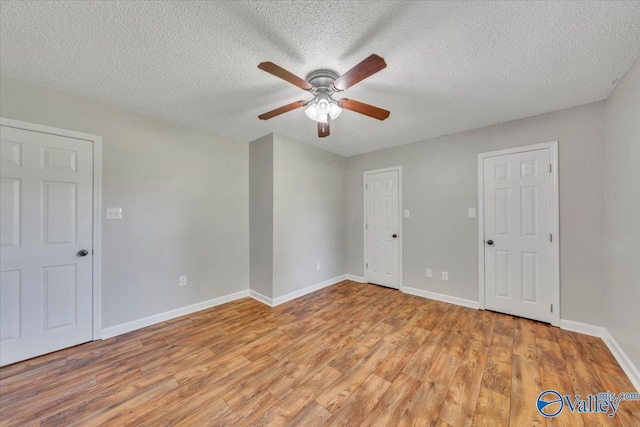 empty room featuring a textured ceiling, light wood finished floors, baseboards, and a ceiling fan