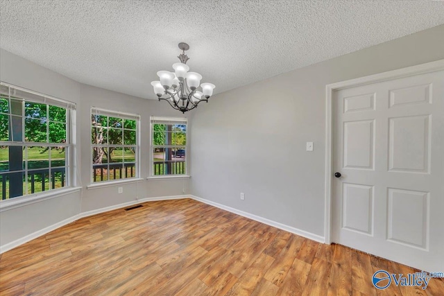 empty room featuring light wood-style flooring, an inviting chandelier, visible vents, and a wealth of natural light