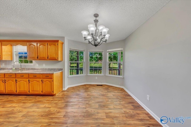 kitchen featuring an inviting chandelier, a sink, light countertops, light wood-type flooring, and brown cabinets