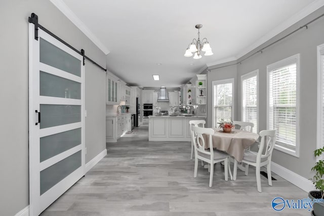 dining space featuring a barn door, light hardwood / wood-style flooring, ornamental molding, and an inviting chandelier