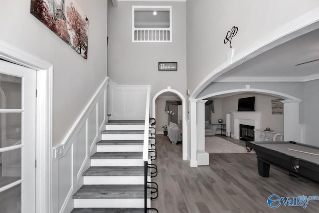 staircase with a towering ceiling, ornate columns, ornamental molding, hardwood / wood-style flooring, and billiards