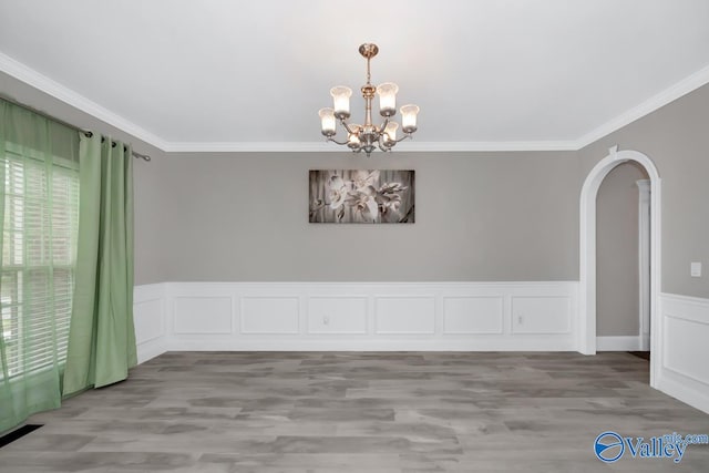 empty room with wood-type flooring, an inviting chandelier, and crown molding