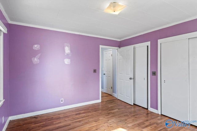 unfurnished bedroom with ornamental molding, multiple closets, and hardwood / wood-style flooring